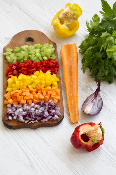 Chopped fresh vegetables (carrot, celery, onion, colored peppers) arranged on cutting board on white wooden table, low angle view. - Photo, Image