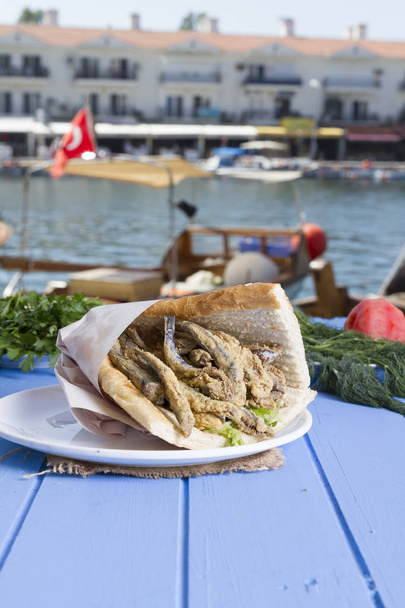 トルコの伝統的なおいしい深い乾燥したヨーロッパ アンチョビ フィッシュ ・ サンドイッチ スライスした素朴な背景の表に丸いプレートは、青トマト、ルッコラのサラダ、白ねぎ、レモン料理の食材。コピー スペース - 写真・画像