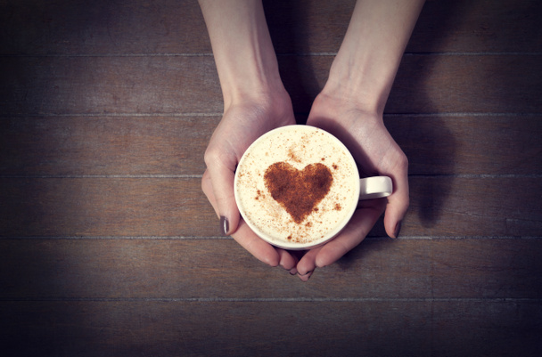 γυναίκα που κρατά ζεστό φλιτζάνι καφέ, με σχήμα καρδιάς - Φωτογραφία, εικόνα