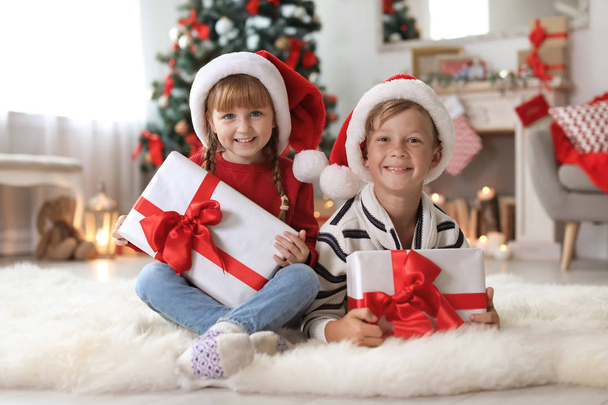 Cute little children in Santa hats with Christmas gift boxes at home - Foto, Bild