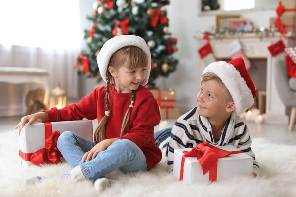 Cute little children in Santa hats with Christmas gift boxes at home - Foto, afbeelding