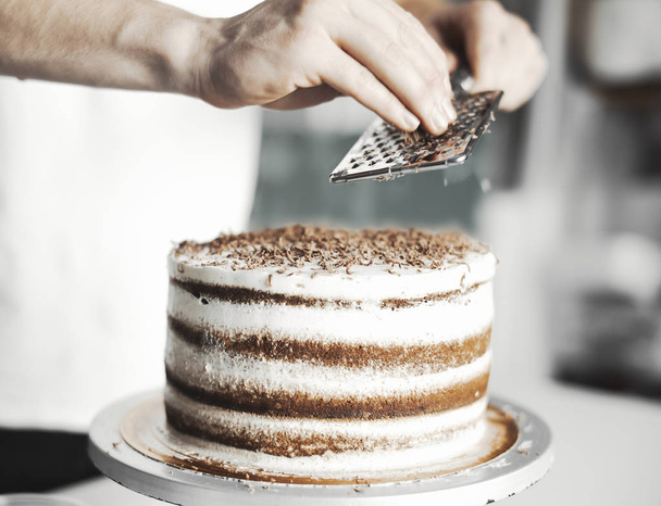 Close up of young attractive cook decorating cake with chocolate. - Foto, immagini