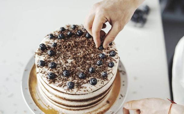 Close up of young attractive cook decorating cake with berries. - Foto, Bild