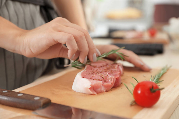 Female chef preparing meat on wooden board at table, closeup - Foto, afbeelding