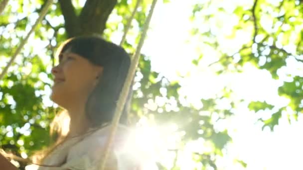 meisje op schommel onder een eikenboom in de zon, vertraagd, close-up schommels - Video