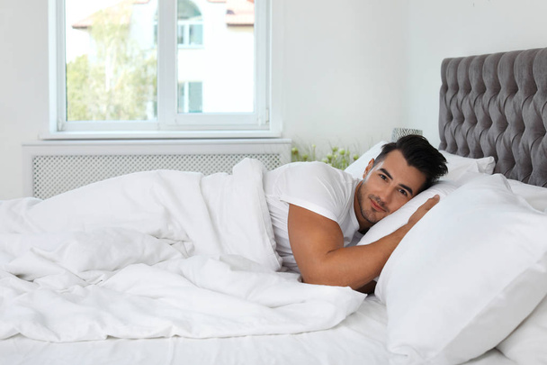 Young man lying in bed with soft pillows at home - Foto, Imagem