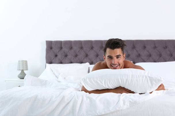 Sexy jeune homme avec oreiller doux sur le lit à la maison
 - Photo, image