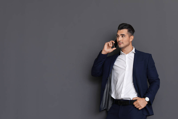 Handsome young man talking on phone against grey background. Space for text - Φωτογραφία, εικόνα