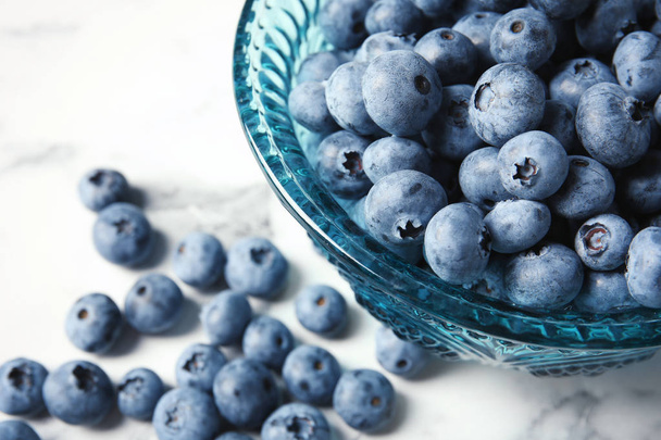 Bowl with fresh blueberries on marble table, closeup - 写真・画像