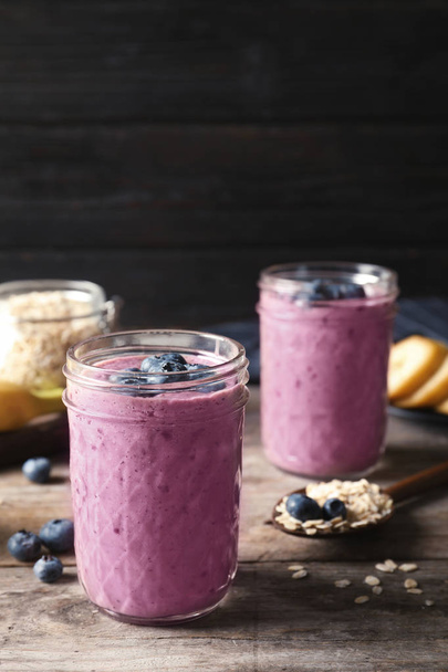 Jars with blueberry smoothies on wooden table - Fotoğraf, Görsel