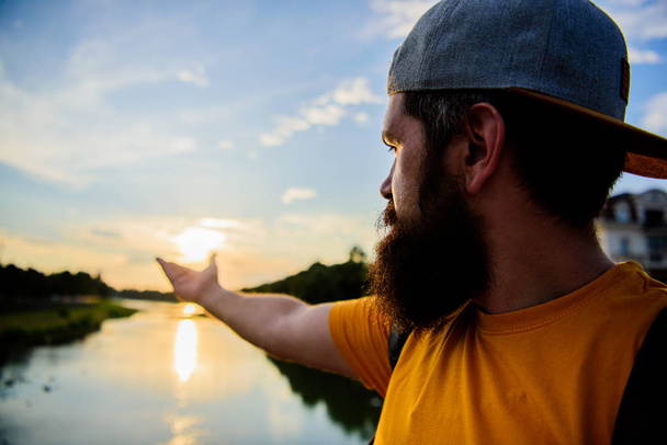 Take moment to admire sunset nature beauty. River sun reflection. Man in cap enjoy sunset while stand on bridge. Enjoy pleasant moment. Guy in front of blue sky at evening time admire landscape - Fotoğraf, Görsel