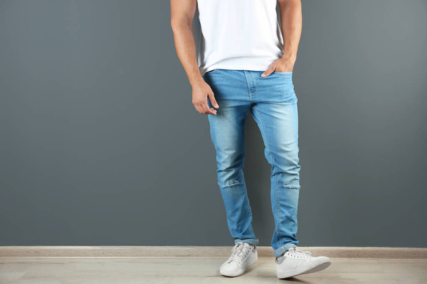Young man in stylish jeans near grey wall with space for text, focus on legs - 写真・画像