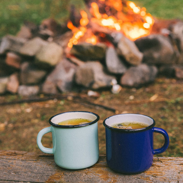 two metal cups with tea. fire on background. union with nature - Photo, Image