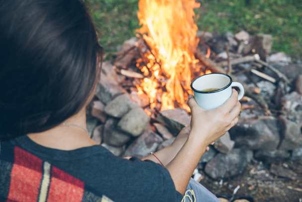 woman sitting near fire with cup of tea. hiking concept - Foto, Imagen