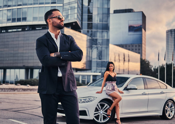 Couple attrayant bien habillé près d'une voiture de luxe à l'extérieur contre un gratte-ciel
. - Photo, image