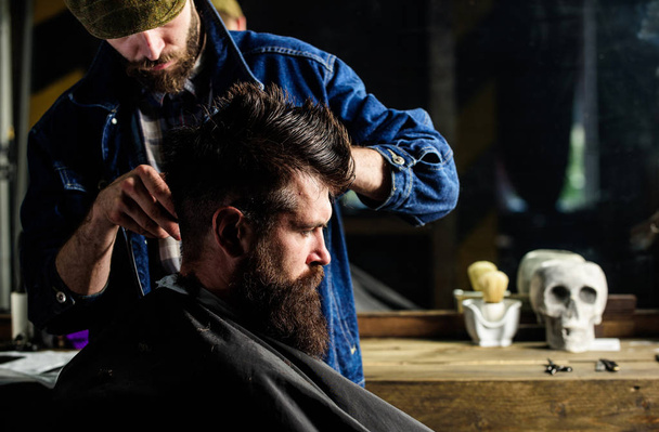 Hipster client getting haircut. Barber styling hair of brutal bearded client with clipper. Haircut concept. Barber with hair clipper works on hairstyle for man with beard, barbershop background - 写真・画像