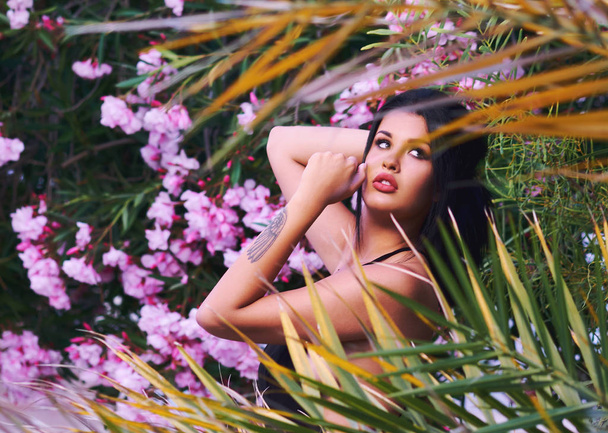 Retrato en la cabeza de una joven morena sexy posando al aire libre. Chica posan cerca de florecer hermosas flores y hojas de color rosa brillante. Mujer de 20-25 años. Humor romántico, sensual, verano
 - Foto, Imagen