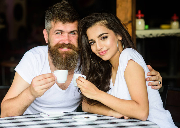Pleasant family moment. Couple in love drink black espresso coffee in cafe. Enjoy moment with cup of coffee drink. Man with beard and attractive happy smiling girl hugs and drinking coffee - Fotó, kép
