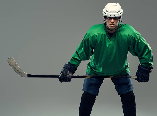 Portrait of a professional hockey player wearing full gear and hockey stick. Isolated on a gray background. - Photo, Image