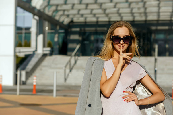 Delightful blonde girl wearing sunglasses and showing silence gesture. Empty space - Photo, Image