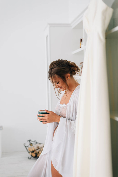 Uma menina em um vestido de baile branco está tomando café da manhã e bebendo uma xícara de café desde a manhã de bom humor
 - Foto, Imagem