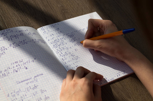 Ženská ruka píše matematické vzorce v poznámkovém bloku. Domácí škola v matematice - Fotografie, Obrázek