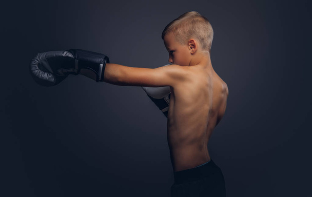Przystojny chłopak bokser z blond włosy, noszenie rękawic bokserskich treningu w studio. Na białym tle na ciemnym tle. - Zdjęcie, obraz