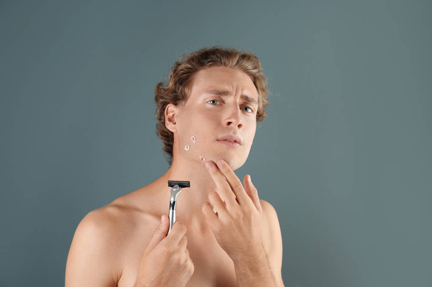 Young man with face hurt while shaving on gray background - Foto, imagen