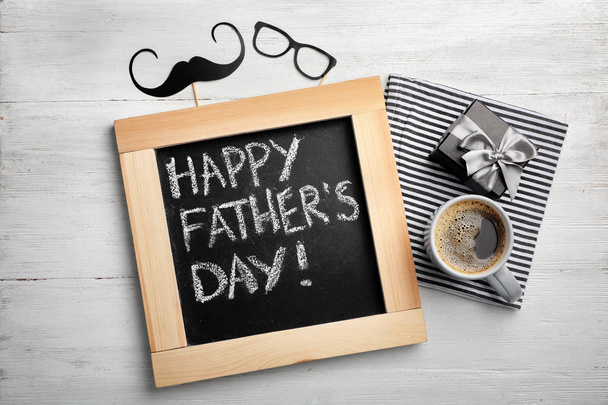 Flat lay composition with chalkboard, cup of coffee and gift box on wooden background. Father's day celebration - Foto, imagen