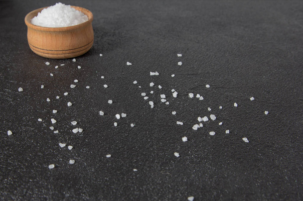 Sea salt in a wooden bowl on a dark concrete background. Crystals of salt on a dark cement background. - Photo, Image