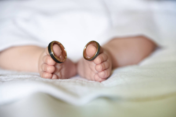 Feet of a newborn wearing his parents' wedding rings on his big toes - Foto, imagen