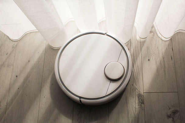 Robotic vacuum cleaner cleans the room from dust and debris, light from the window - Foto, Imagen