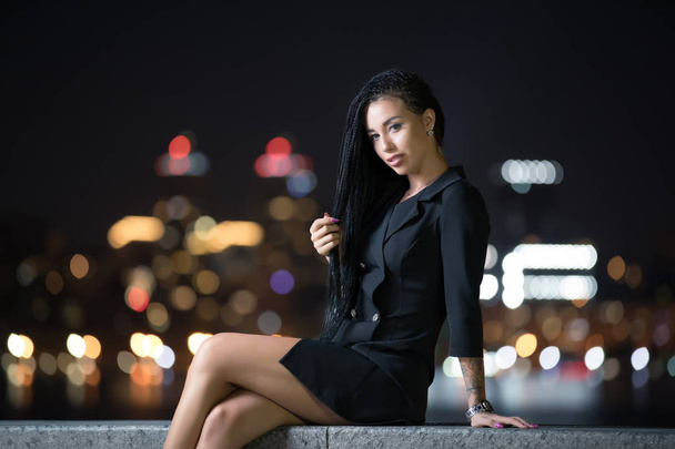 Sexy woman sitting on fence in night city - Zdjęcie, obraz