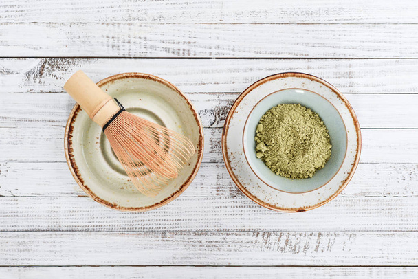 Matcha green tea in powder and bamboo whisk on white wooden background. Top view.  - Valokuva, kuva