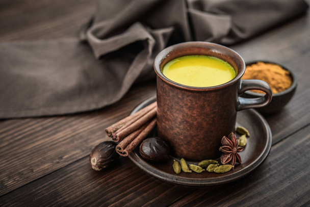 Traditional Indian drink turmeric milk is golden milk with cinnamon, cloves, pepper and turmeric on a wooden background with spices  - Foto, Bild