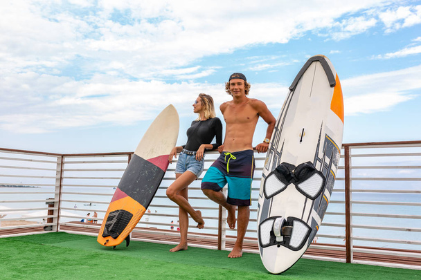 Mosolygó fiatal aktív pár szörfösök pihentető a strandon után a sport, szörf. Egészséges életmód. Extrém vízisportok - Fotó, kép