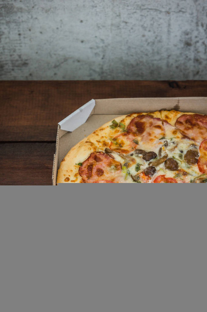 Pizza on wooden background in rustic style. Italian pizza from the shop in a cardboard box. Simple food on a wooden background - Photo, image
