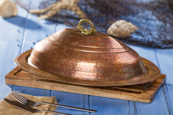 Bandeja de cobre tradicional turca y árabe con tapa en tabla de cortar de bambú que sirve con red de pesca
 - Foto, Imagen