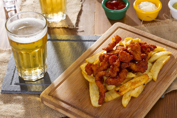 Cold Foamy Golden Chilled Glass of Draft Beer Served with Delicious Hot Crispy Homemade Fresh Fried Plate in Chicken Wings, Sliced Pork Sausage and Fries - Photo, Image