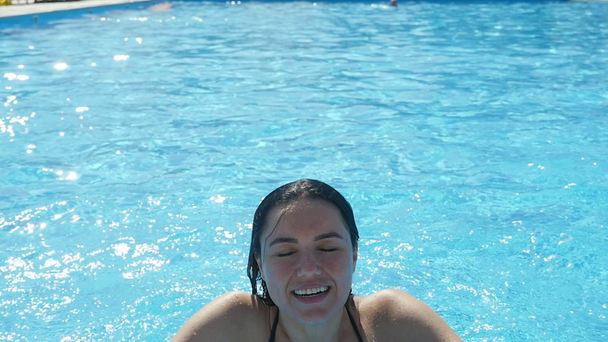 Happy young woman jumping cheery at th edge of a swimming pool in slow motion                             An exciting view of a smiling young woman in black bikini jumping hilariously at the edge of a pool with sparkling celester waters in slo-mo - Πλάνα, βίντεο