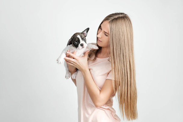 A beautiful young girl is holding a puppy of a French bulldog. - Фото, изображение