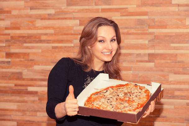 Bright adult woman with pizza in box holding thumb up and smiling at camera - 写真・画像