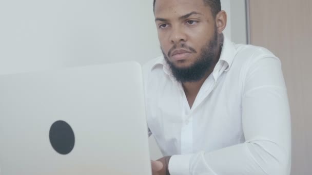 Ein ernsthafter schwarzer Mann arbeitet mit einem Computer, der im Büro auf den Monitor schaut. Afrikanischer amerikanischer Geschäftsmann besorgt am Laptop. - Filmmaterial, Video