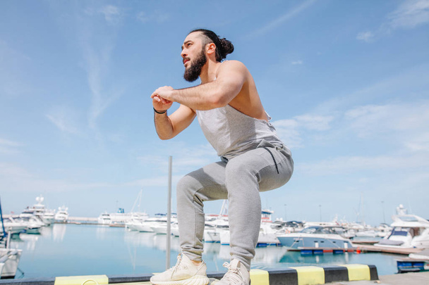 Fitness athlete doing jump squats on makeshift plyo-box on summer sea pier - Valokuva, kuva
