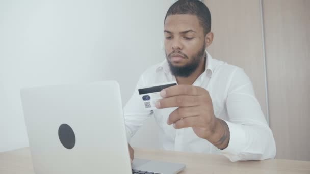 Afryki młody człowiek zakupy online z karty kredytowej za pomocą laptopa w domu. - Materiał filmowy, wideo