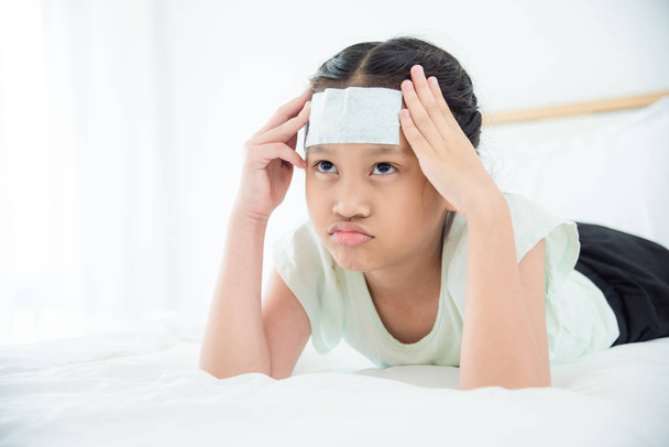 Jovem asiático com gel fresco na testa com dor de cabeça deitado na cama
 - Foto, Imagem