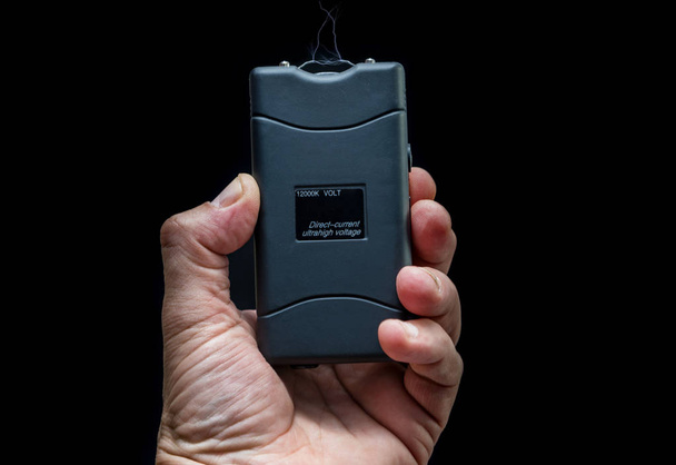 Рука держит электрошокер на черном фоне
 - Фото, изображение