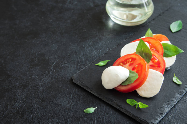 Traditional Italian Caprese Salad - sliced tomatoes, mozzarella cheese and basil on dark stone background, top view, copyspace. Caprese Salad, italian mediterranean food. - Valokuva, kuva