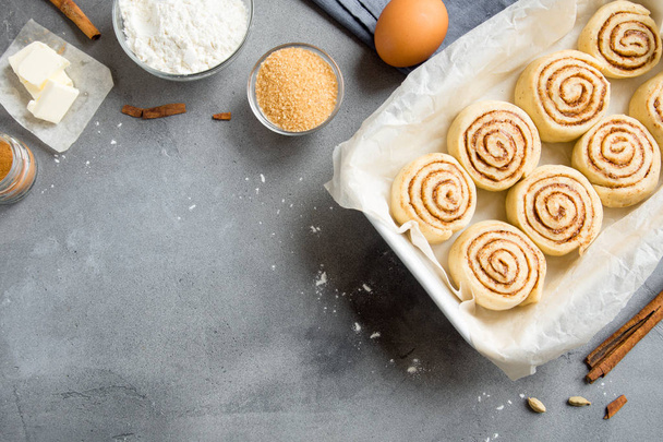 Cinnamon rolls or cinnabon, homemade recipe raw dough preparation sweet traditional dessert buns with pastry ingredients on grey stone background, copy space. - Фото, зображення