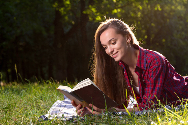 young woman reading book in park at daytime - Фото, изображение